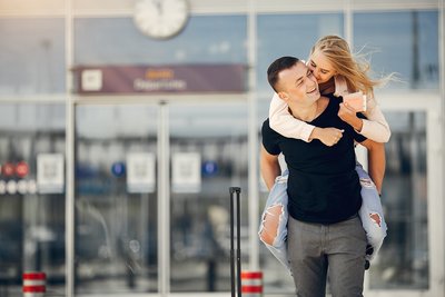 Mann trägt eine Frau auf dem Rücken. Sie hält ein Reisepass in der Hand. Beide lächeln