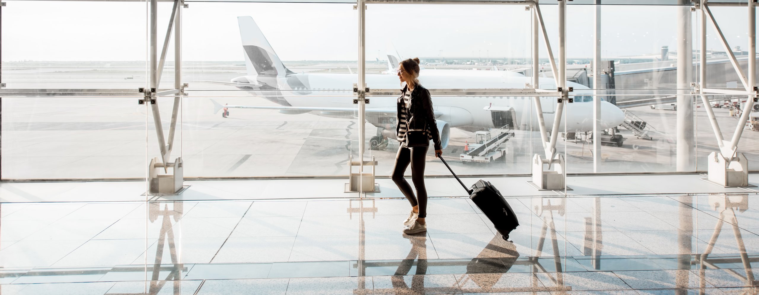 Man sieht ein Mann der einen Koffer hinter sich herzieht am Flughafen. Im Hintergrund ist ein Flugzeug zu sehen